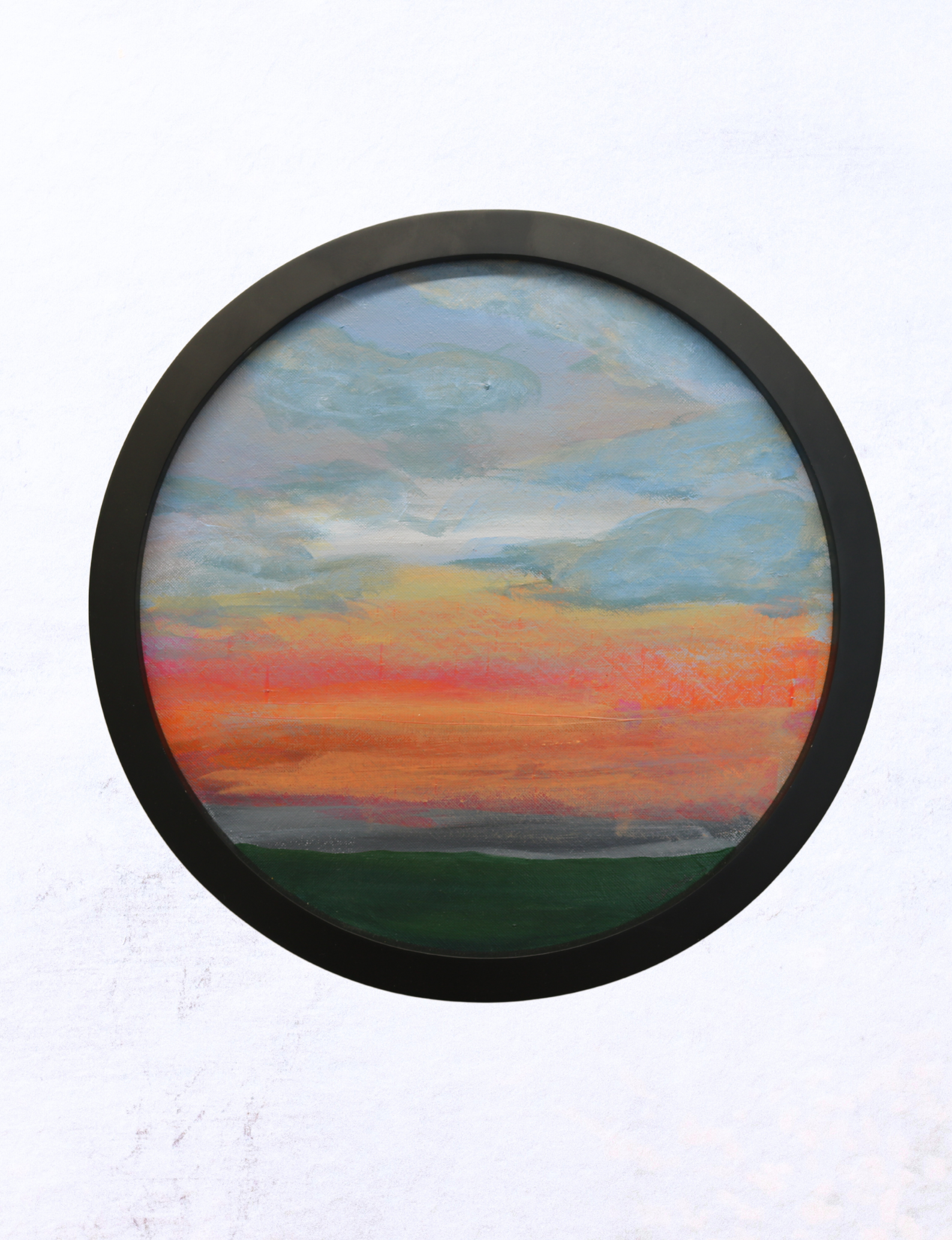 Image is of a round painting in a chunky black wooden frame. The painting, which is acrylic on canvas board , is of a distant view towards the North Yorkshire Moors. in the foreground at the bottom of the canvas is the dark green of the hedgerows and trees, above the sunrise is depicted firstly with a soft hazy grey above the tree line and then erupts into vibrant oranges and pinks up to the centre of the canvas. The top half of the canvas shows a rolling cloudy sky with blues, greys, whites and lilacs.