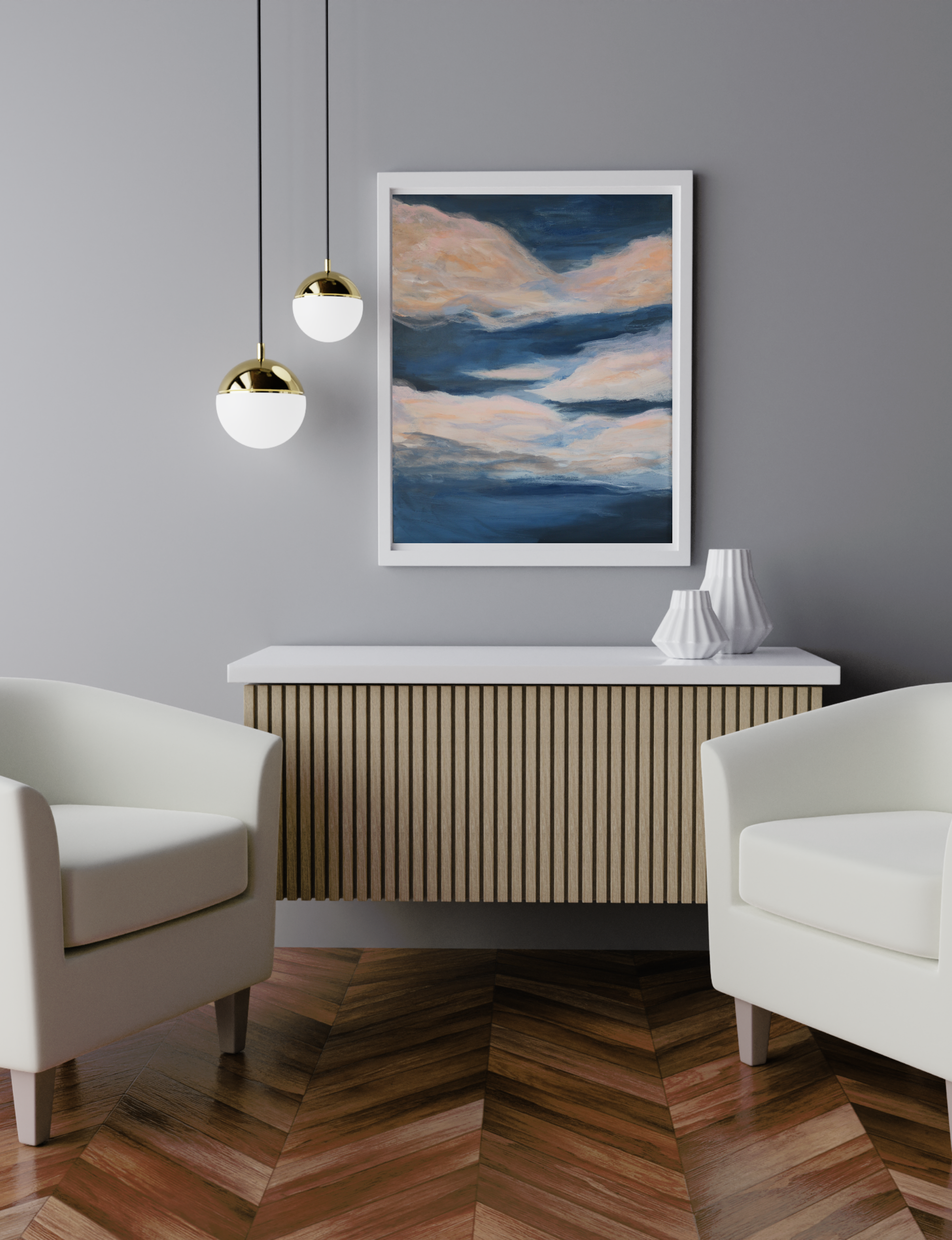 The image shows 'First Light', an acrylic on canvas by Kate Brown, mounted in a white frame against a soft grey wall. To the left of the painting are two pendant lights and below is a console table with white top and vertical slatted wooden front. Either side of the table are soft white bucket armchairs and the floor is wooden parquet.